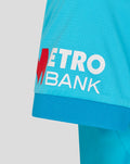 Blue women's ODI cricket shirt sleeve with Metro Bank logo and red M emblem.