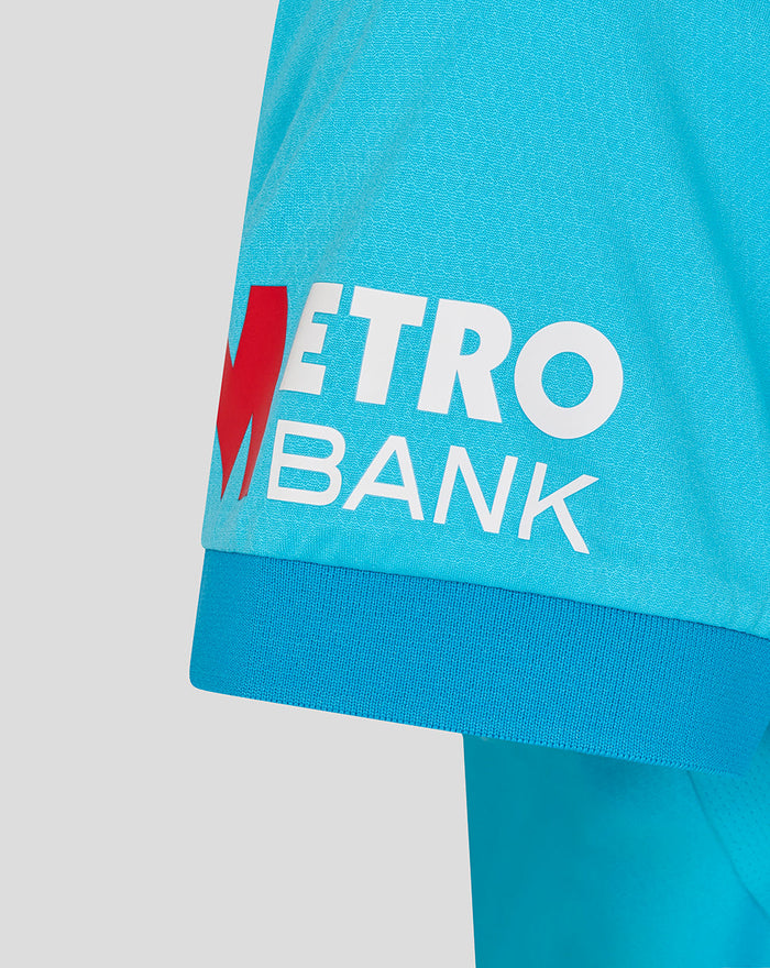 Blue women's ODI cricket shirt sleeve with Metro Bank logo and red M emblem.