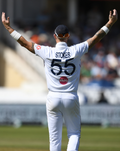 Cricket player in white England Test shirt, back view with Stokes 55 and navy crest, arms raised.