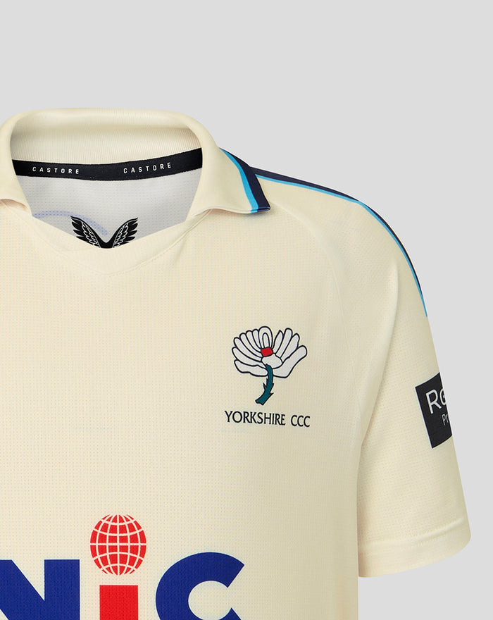 Cream cricket jersey front close up with Yorkshire CCC crest and bold blue sponsor lettering across the lower front