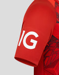 Close up of red cricket jersey sleeve with bold white letters on textured fabric.