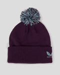 Dark purple ECB training bobble hat with teal faux fur pom and Castore logo on the cuff